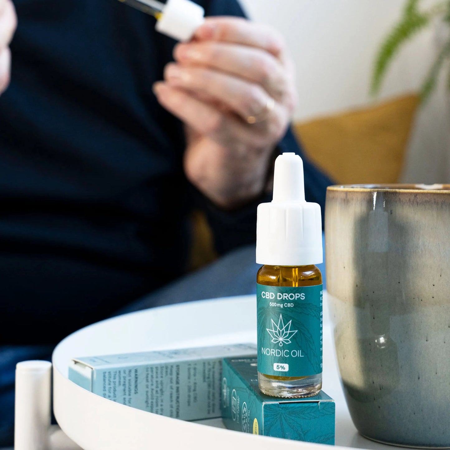 CBD-drops flaske fra Nordic Oil på bordet ved siden af æsker.