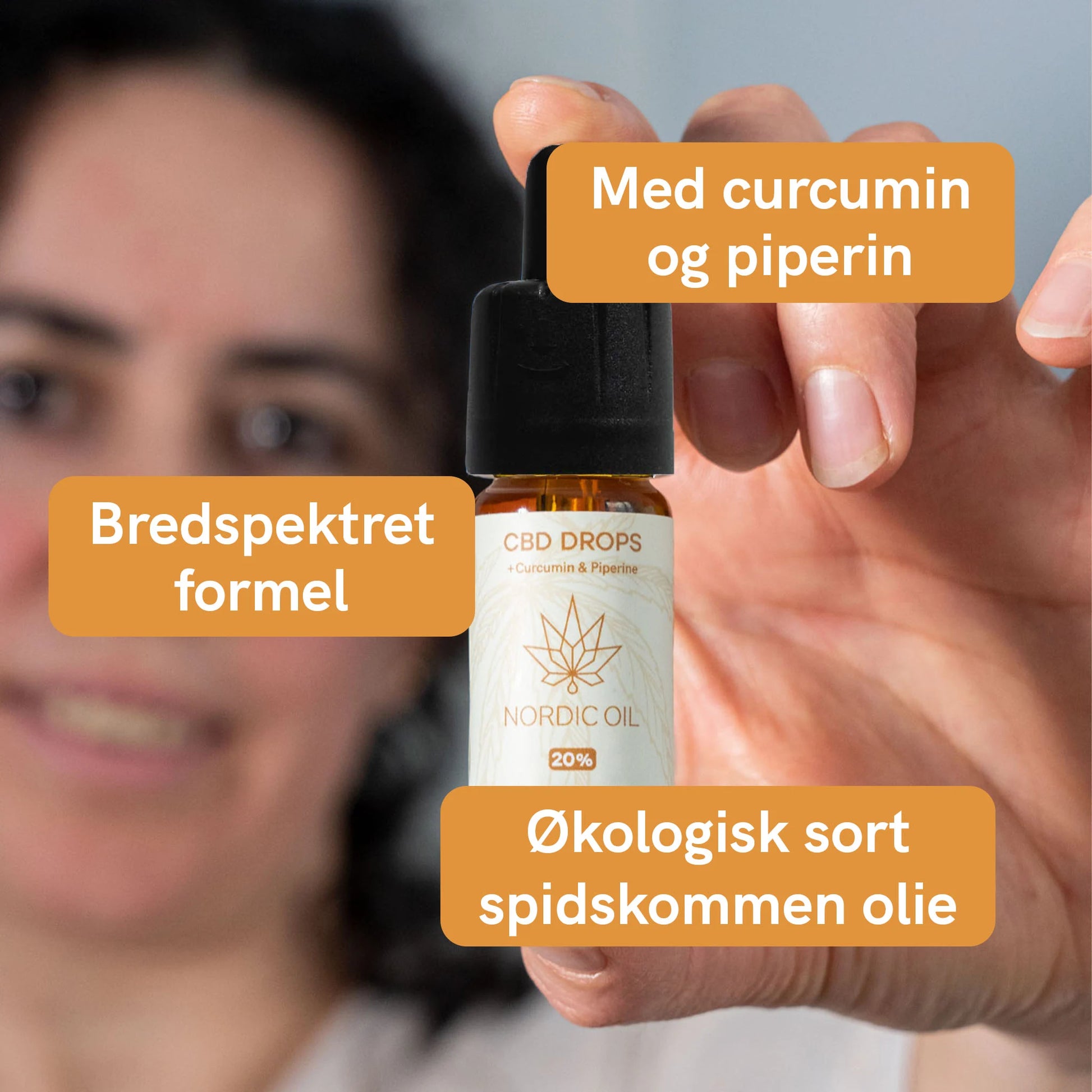 Nærbillede af en hånd, der holder en flaske CBD-dråber fra Nordic Oil med orange etiketter.