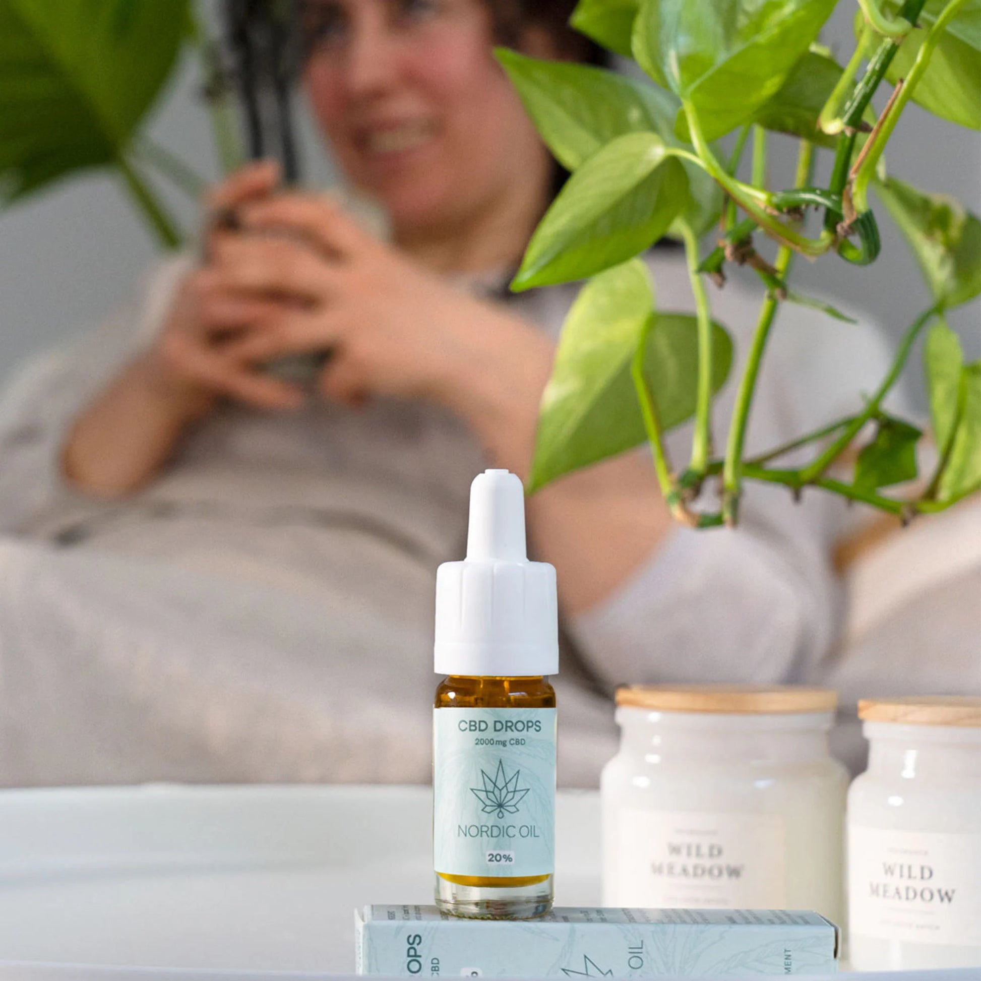 CBD-drops flaske fra Nordic Oil på bordet med grønne planter og hudplejeprodukter i baggrunden