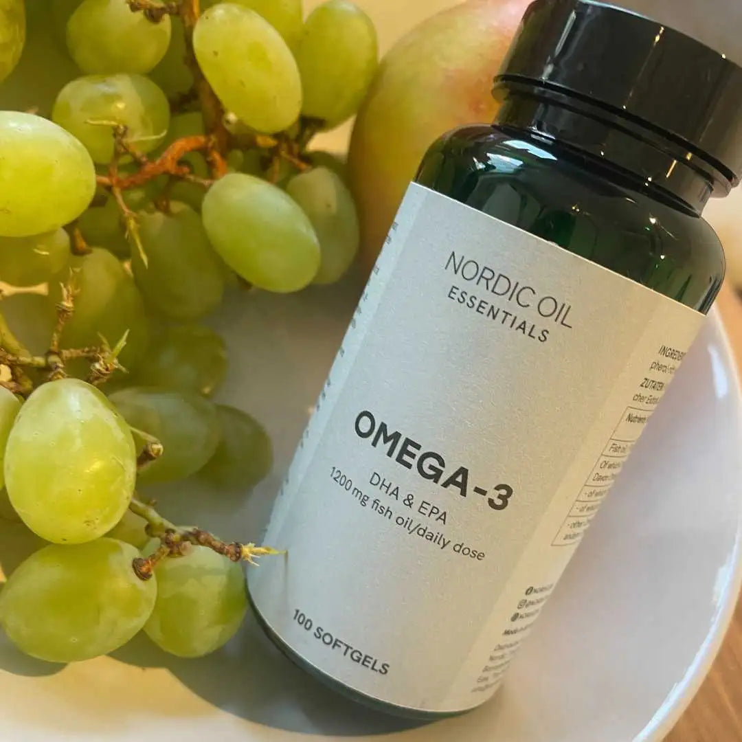 Nordic Oil Essentials Omega-3 tilskud i glasflaske ved siden af grønne druer