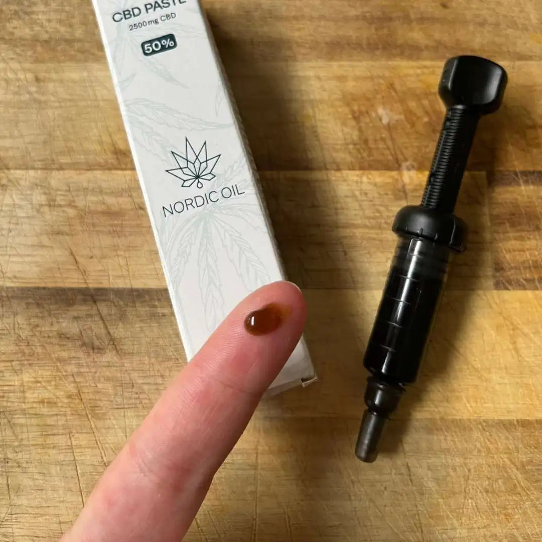 Nordic Oil CBD-pasteboks og dropper på træbord med en finger, der har en dråbe CBD-paste