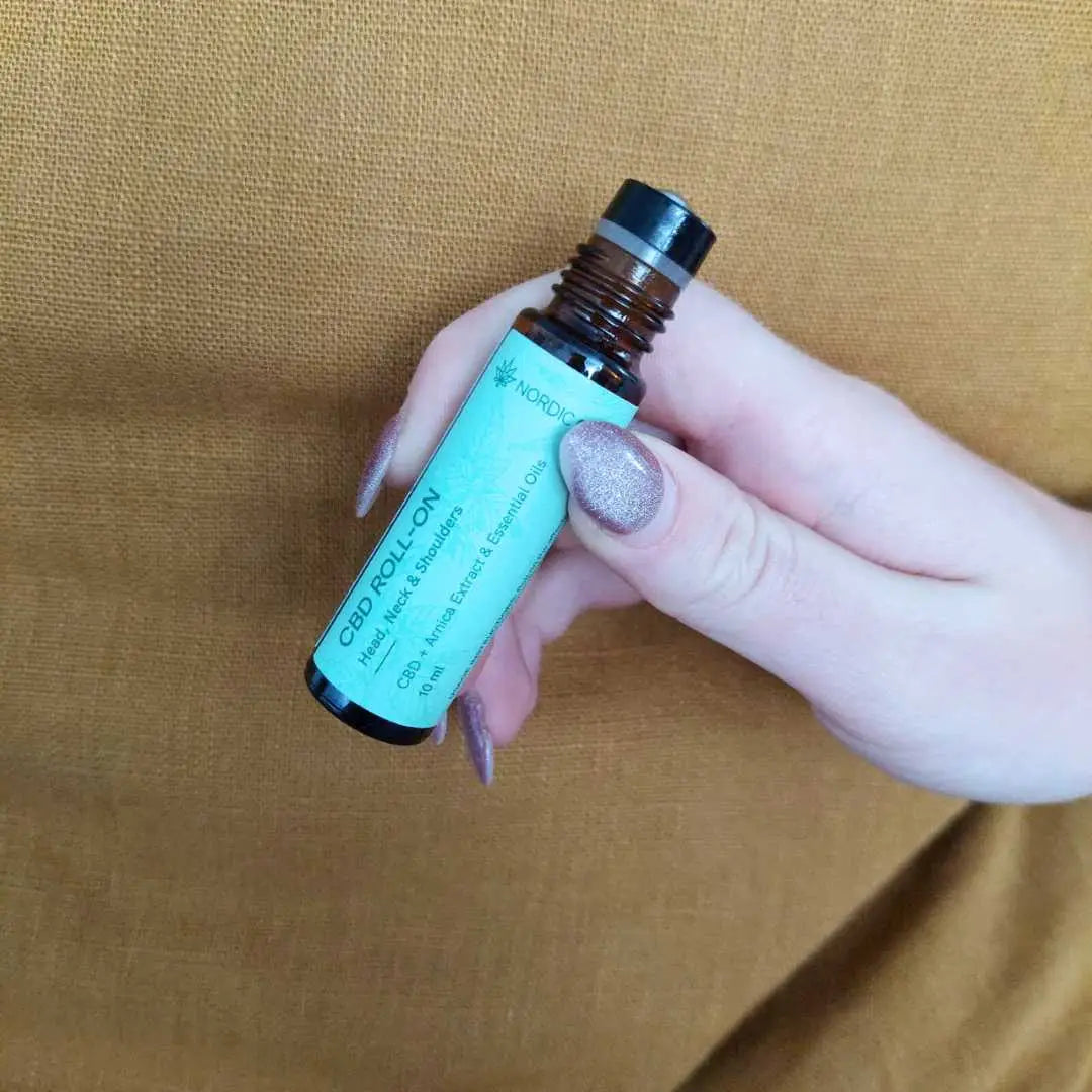 Hånd der holder en CBD-roll-on olieflaske med turkis etiket