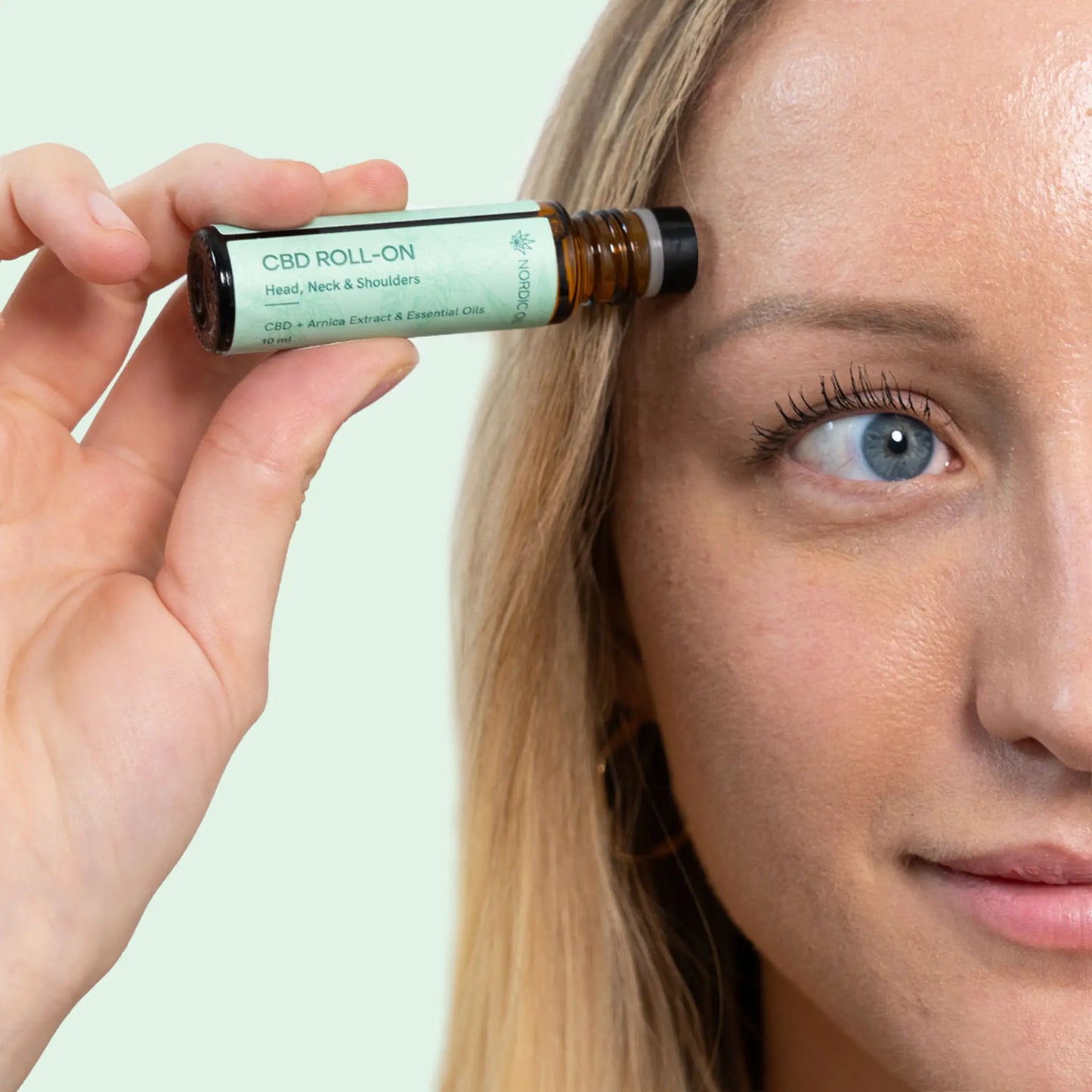 CBD-roll-on olie til hoved, nakke og skuldre holdes tæt ved en persons ansigt.