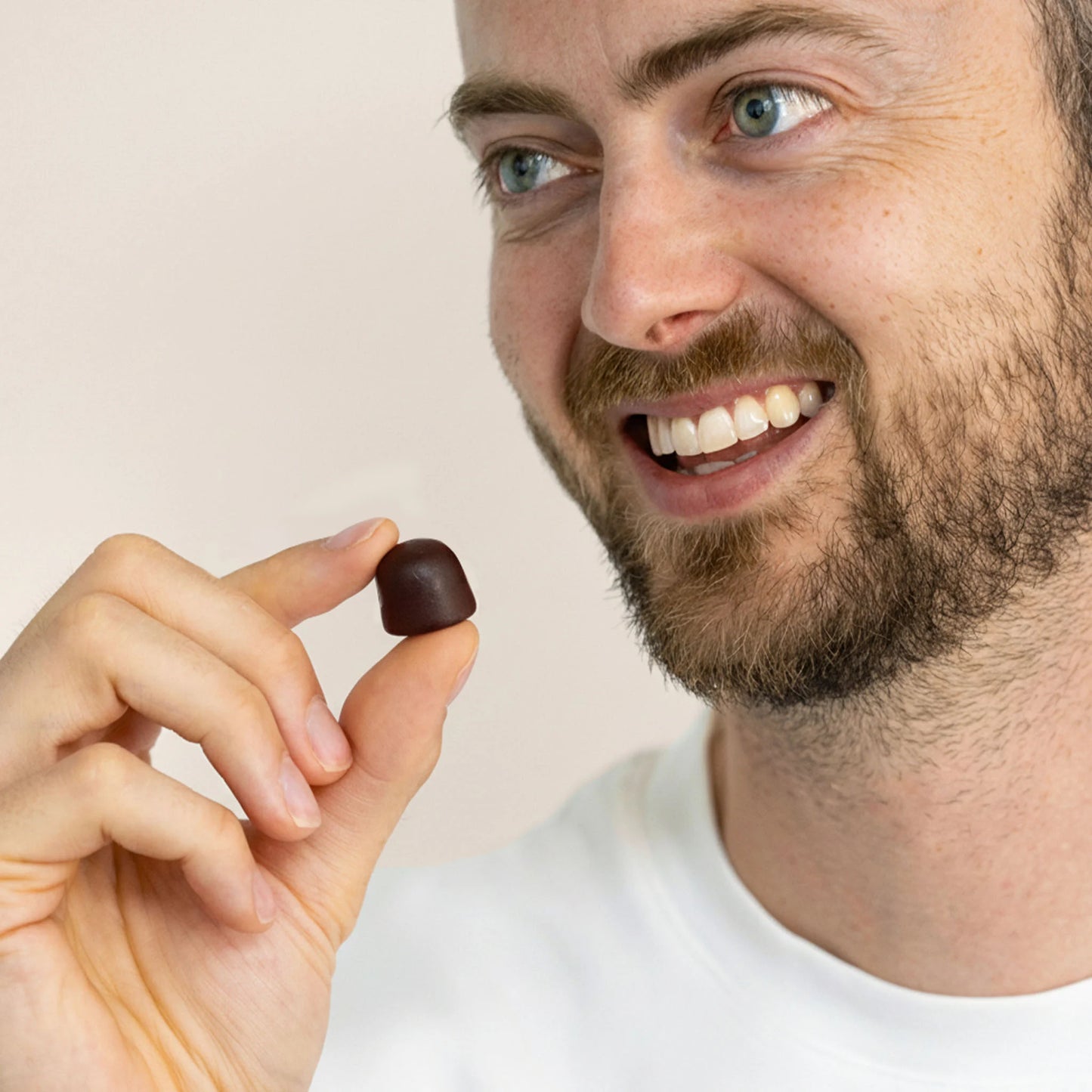 Mand holder en mørkebrun shilajit gummier mellem fingrene og smiler.