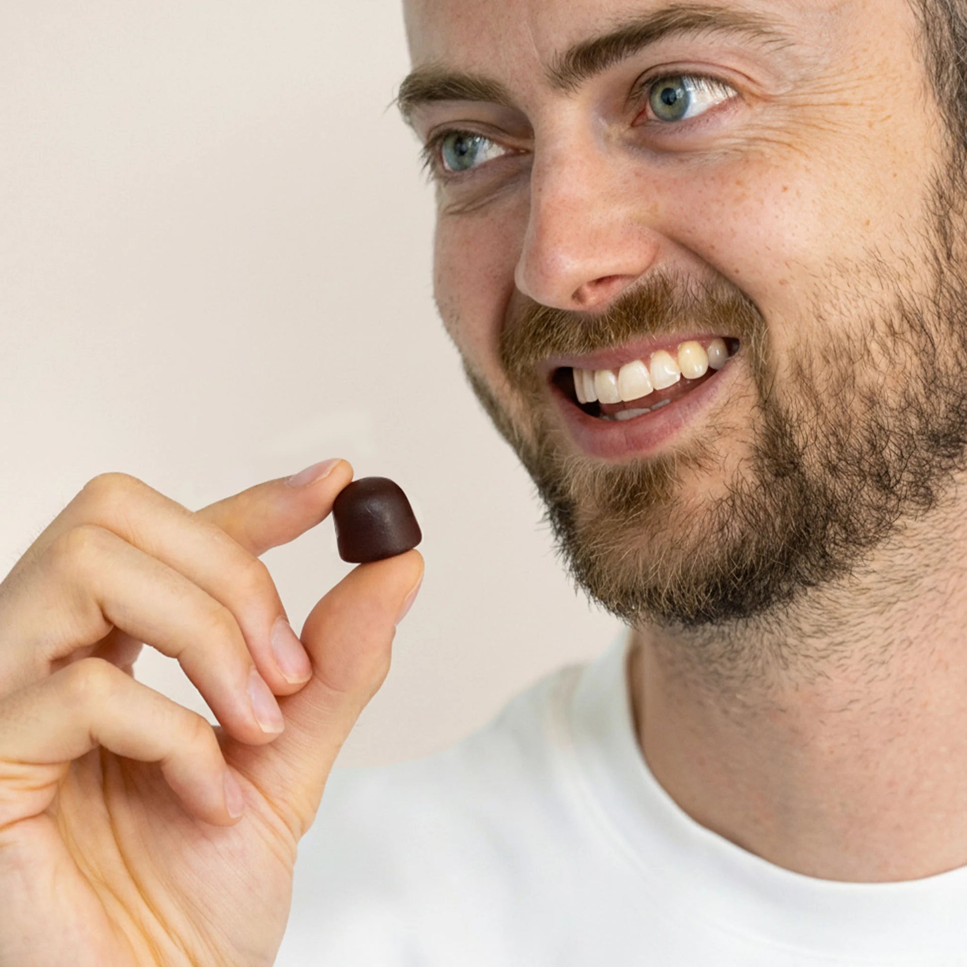 Mand holder en mørkebrun shilajit gummier mellem fingrene og smiler.
