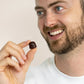 Mand holder en mørkebrun shilajit gummier mellem fingrene og smiler.