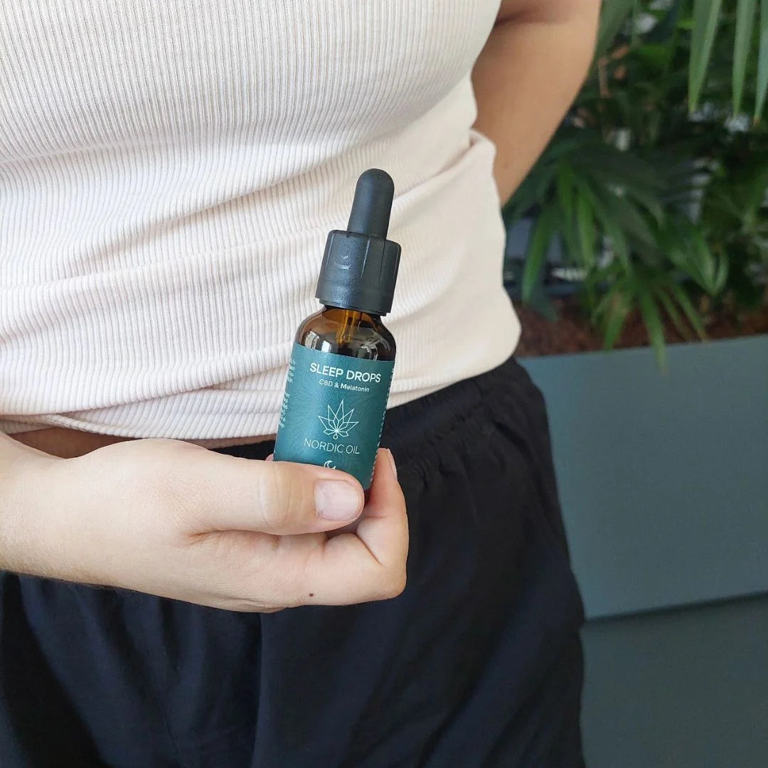 Hånd der holder en amber glasflaske med dropper mærket Nordic Oil Sleep Drops CBD og Melatonin.