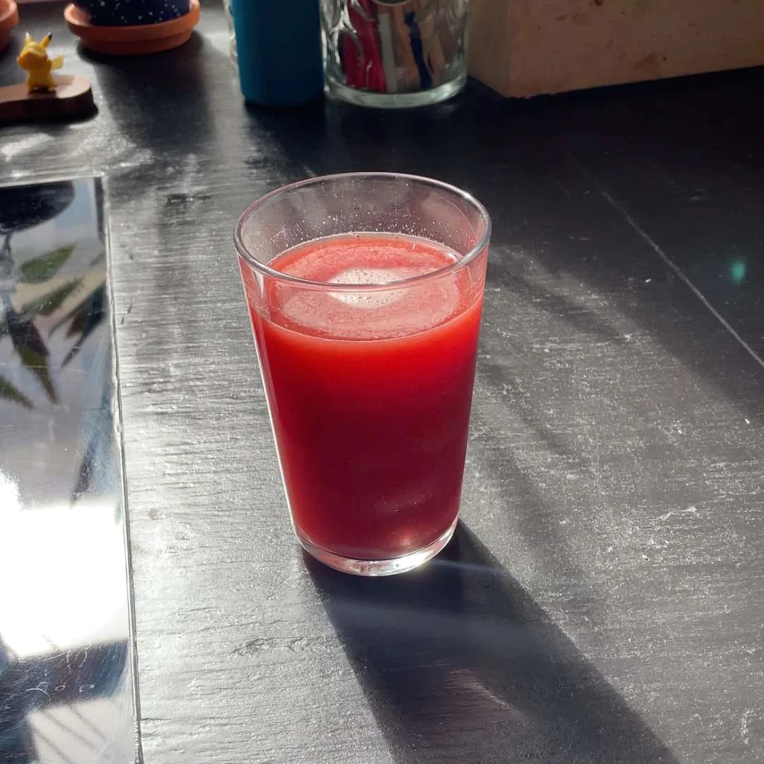 Glas med rød juice på en mørk bordplade i sollys