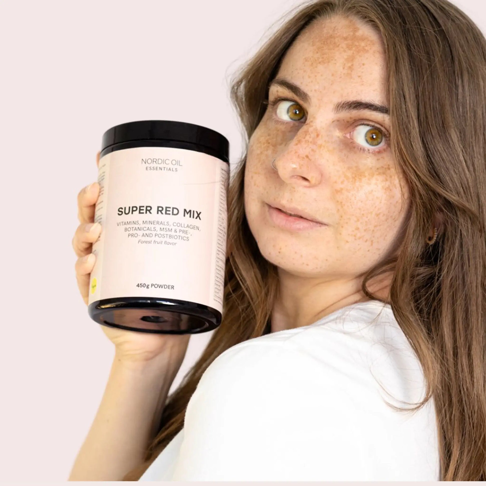Kvinde med fregner holder en lyserød Nordic Oil Essentials Super Red Mix-pulverkrukke